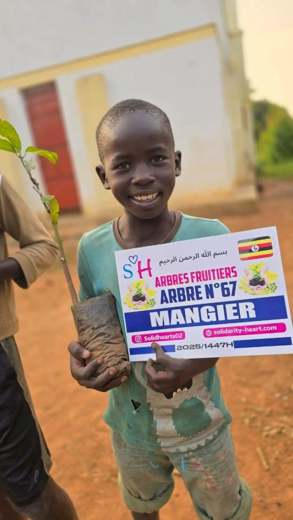 Enfant souriant avec la plaque de plantation d’un manguier.