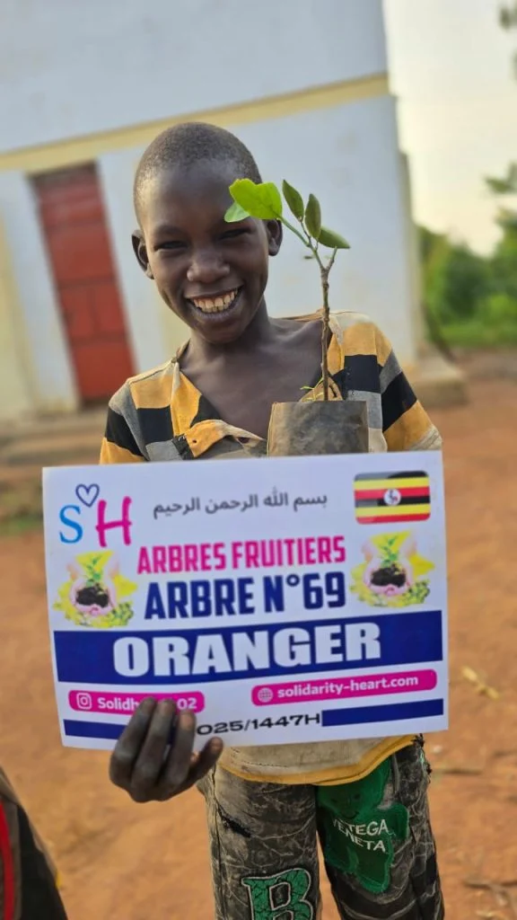 Enfant souriant tenant un plant d’oranger et la plaque du projet.