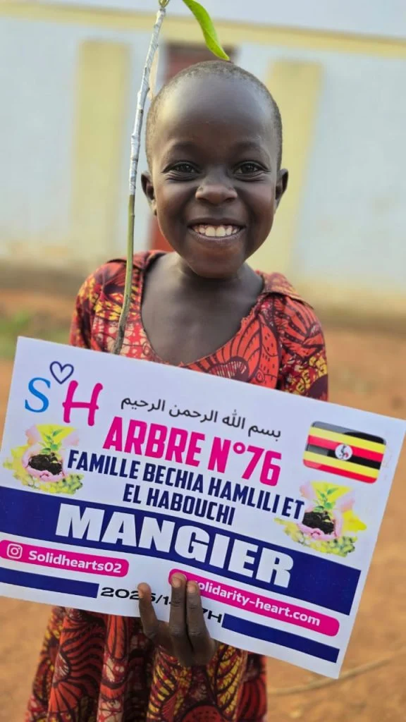 Enfant souriant avec la plaque de plantation d’un manguier.